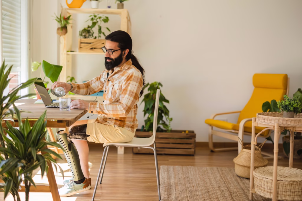 man with computer at home pouring water in a glass